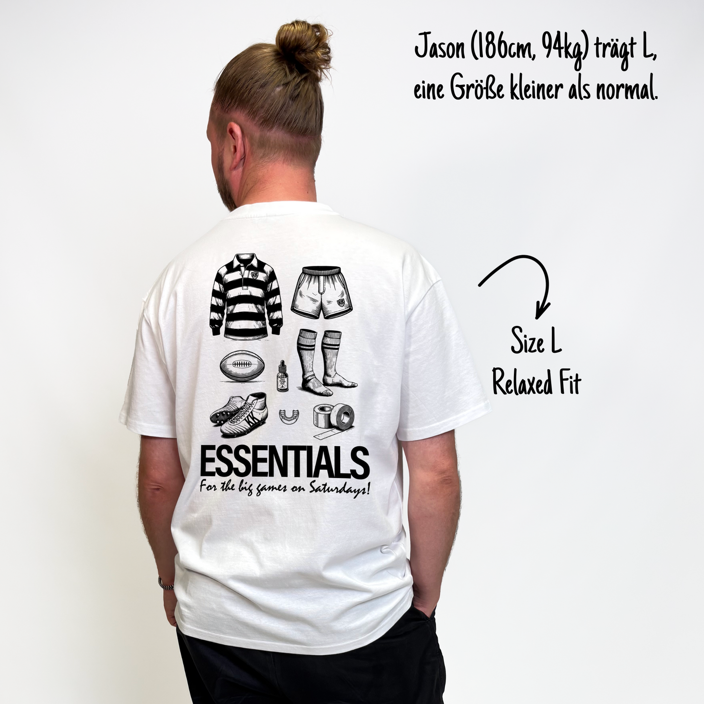 Jason (186cm, 94kg) trägt das weiße Slow Sunday Rugby Club Tee in L. Man sieht das Model von hinten. Er trägt das Shirt im Relaxed Fit, eine Größe kleiner als normal. Das Shirt hat einen großen Print auf dem Rücken: ein Trikot, Shorts, ein Ball, Schuhe, Mundschutz, Tape, Teebaumöl und Stulpen. Untendrunter steht: "Essentials for the big games on Saturdays!"