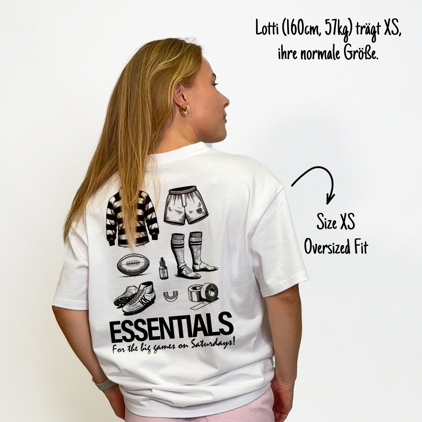 Lotti (160cm, 57kg) trägt das weiße The Essentials Tee in XS. Man sieht das Model von hinten. Das Shirt ist oversized geschnitten und hat einen großen Print auf dem Rücken: ein Trikot, Shorts, ein Ball, Schuhe, Mundschutz, Tape, Teebaumöl und Stulpen. Untendrunter steht: "Essentials for the big games on Saturdays!"