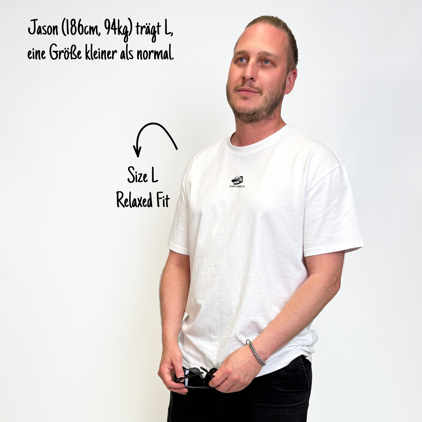 Jason (186cm, 94kg) trägt das weiße Slow Sunday Rugby Club Tee in L. Man sieht das Model von vorne. Er trägt das Shirt im Relaxed Fit, eine Größe kleiner als normal. Das Shirt hat einen kleinen Print auf der Brust: ein Paar Rugby Schuhe und das Schriftlogo Klub Klamotte.