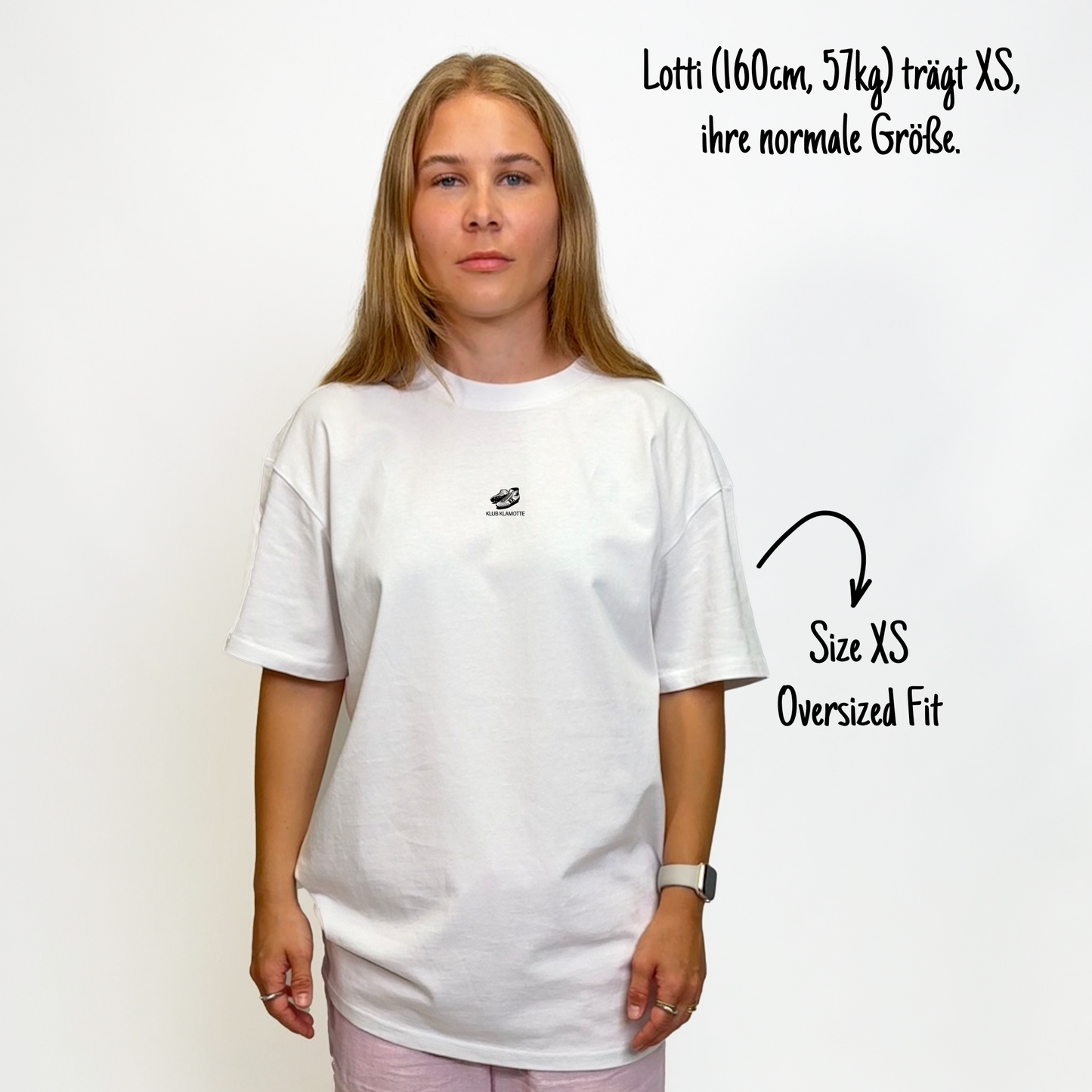 Lotti (160cm, 57kg) trägt das weiße The Essentials Tee in XS. Man sieht das Model von vorne. Das Shirt ist oversized geschnitten und hat einen kleinen schwarzen Print auf der Brust: ein Paar Rugbyschuhe und das Schriftlogo Klub Klamotte.