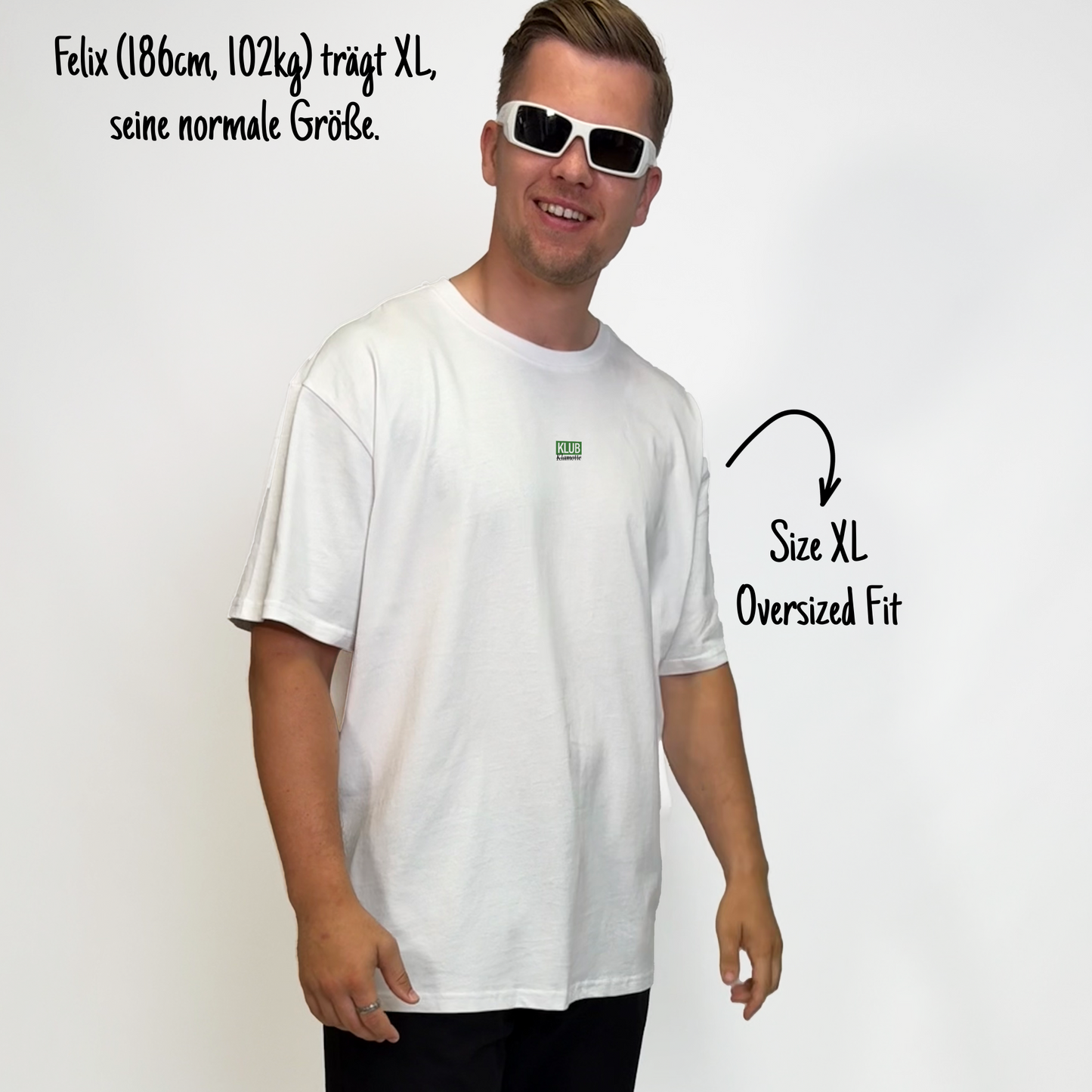 Felix (186cm, 102kg) trägt das weiße Klub Font Tee in XL. Man sieht das Model von vorne. Das Shirt ist oversized geschnitten und hat einen kleinen Print auf der Brust: das Wort KLUB in einem grünen Rechteck hinterlegt und darunter in Schwarz und durchgestrichen Klamotte.