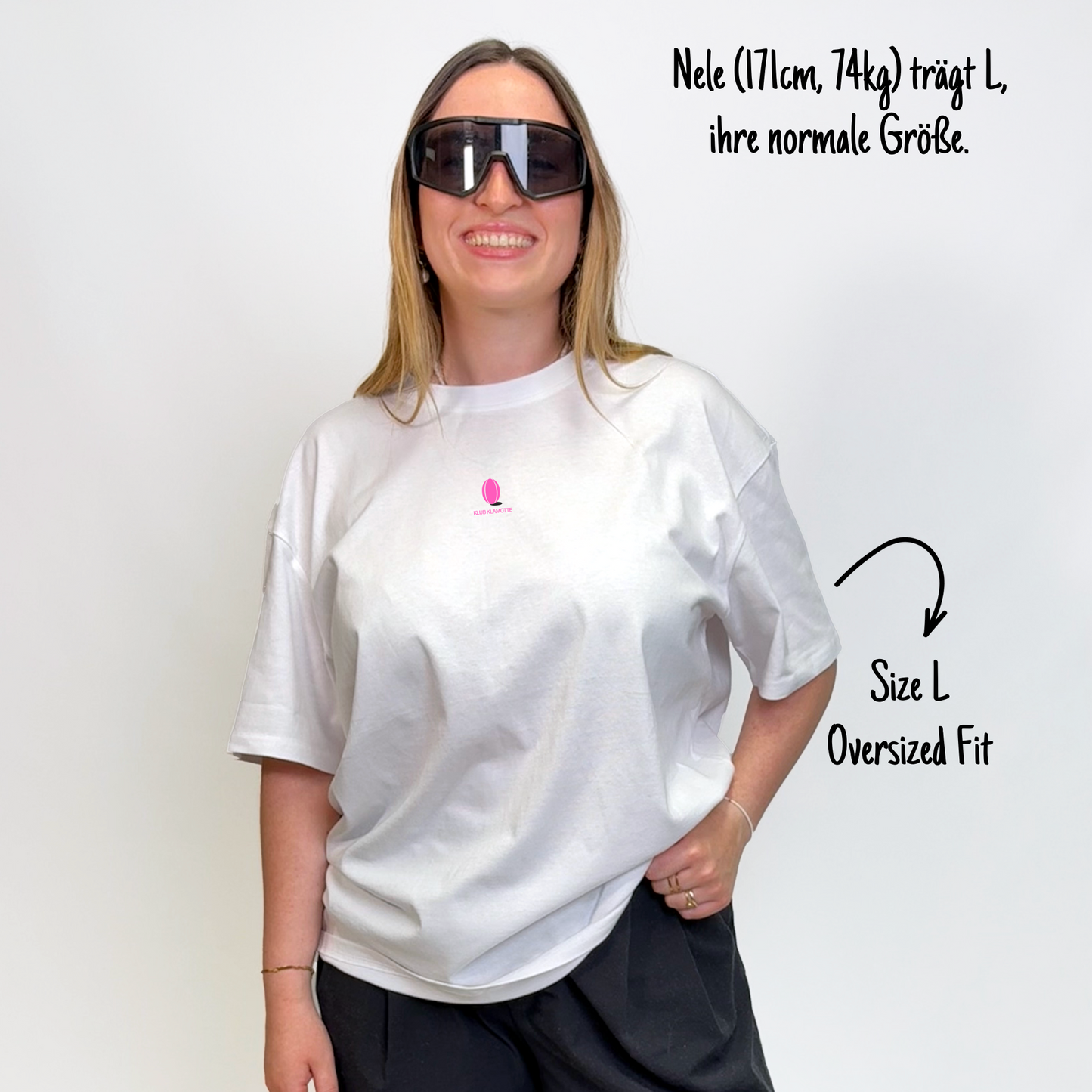 Nele (171cm, 74kg) trägt das weiße Klub Leo Tee in L. Man sieht das Model von vorne. Das Shirt ist oversized geschnitten und hat einen kleinen Print auf der Brust: das pinke Klub Klamotte Logo.