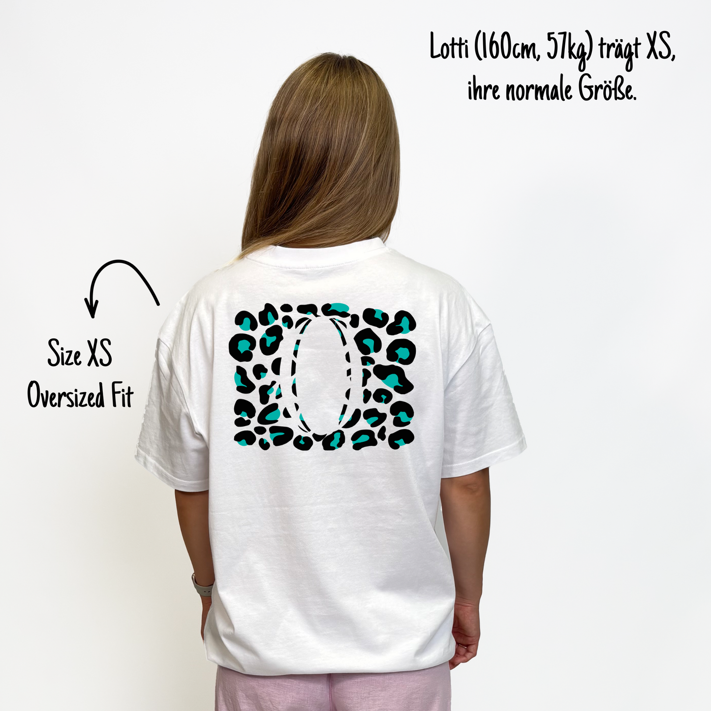 Lotti (160cm, 57kg) trägt das weiße Klub Leo Tee in XS. Man sieht das Model von hinten. Das Shirt ist oversized geschnitten und hat einen großen Print auf dem Rücken: türkise Leoparden-Flecken in einem Rechteck über den ganzen Rücken, in der Mitte ein großer Rugbyball.ausgespart.