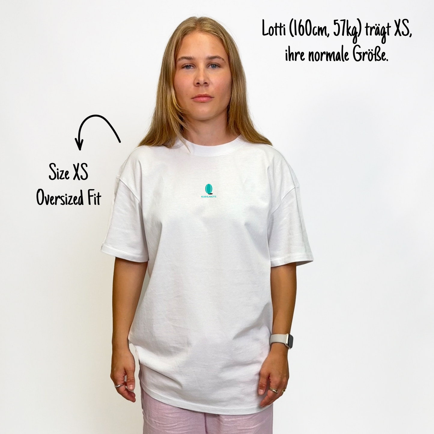 Lotti (160cm, 57kg) trägt das weiße Klub Leo Tee in XS. Man sieht das Model von vorne. Das Shirt ist oversized geschnitten und hat einen kleinen türkisen Print auf der Brust: das Klub Klamotte Logo.