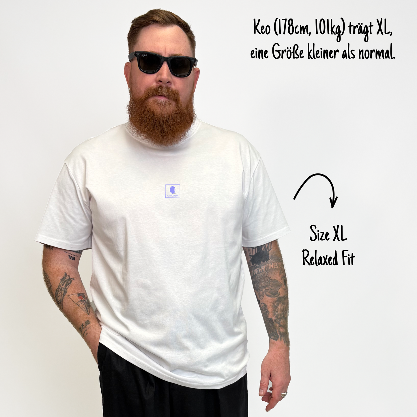 Keo (178cm, 101kg) trägt das weiße Klub Print Tee in XL. Man sieht das Model von vorne. Er trägt das Shirt im Relaxed Fit, eine Größe kleiner als normal. Das Shirt hat einen kleinen lilafarbenen Print auf der Brust: Das Klub Klamotte Logo in einem Quadrat.