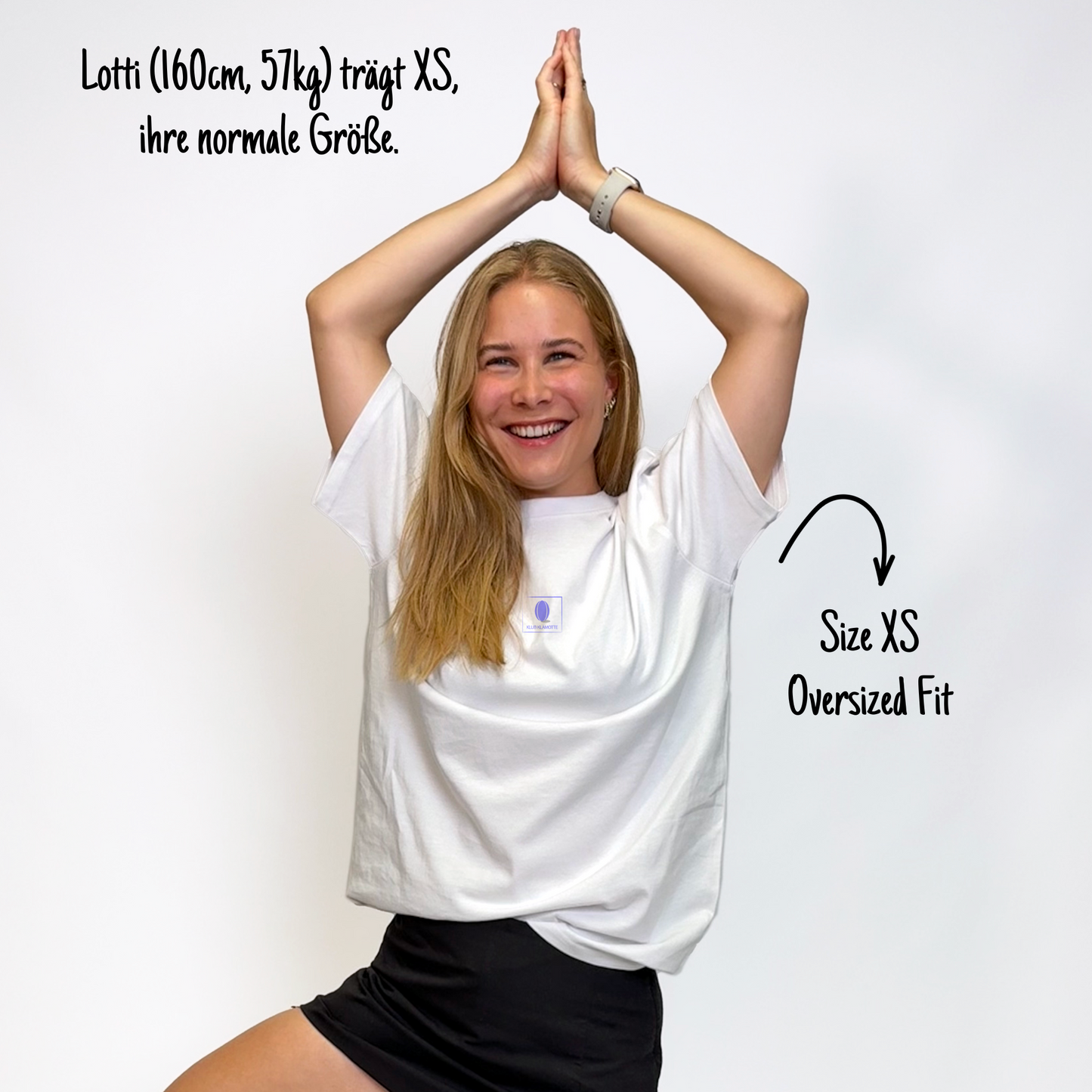 Lotti (160cm, 57kg) trägt das weiße Klub Print Tee in XS. Man sieht das Model von vorne. Das Shirt ist oversized geschnitten und hat einen kleinen lilafarbenen Print auf der Brust: Das Klub Klamotte Logo in einem Quadrat.