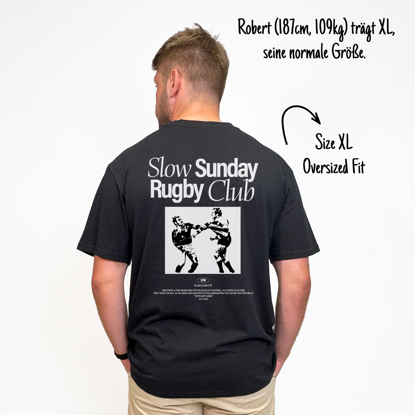 Robert (187cm, 109kg) trägt das schwarze Slow Sunday Rugby Club Tee in M. Man sieht das Model von hinten. Das Shirt ist oversized geschnitten und hat einen großen weißen Print auf dem Rücken: der Schriftzug Slow Sunday Rugby Club Tee und zwei Rugbyspieler im Streit.