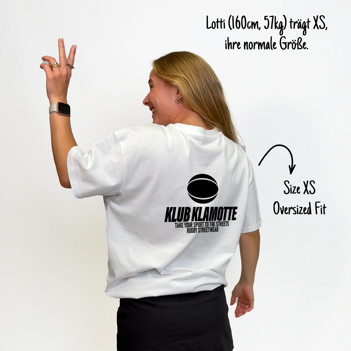 Lotti (160cm, 57kg) trägt das weiße Klub Streets Tee in XS. Man sieht das Model von hinten. Das Shirt ist oversized geschnitten und hat einen großen schwarzen Print auf dem Rücken: ein quer liegender Rugby Ball, darunter der Schriftzug Klub Klamotte und darunter "Take your sport to the streets, Rugby Streetwear".
