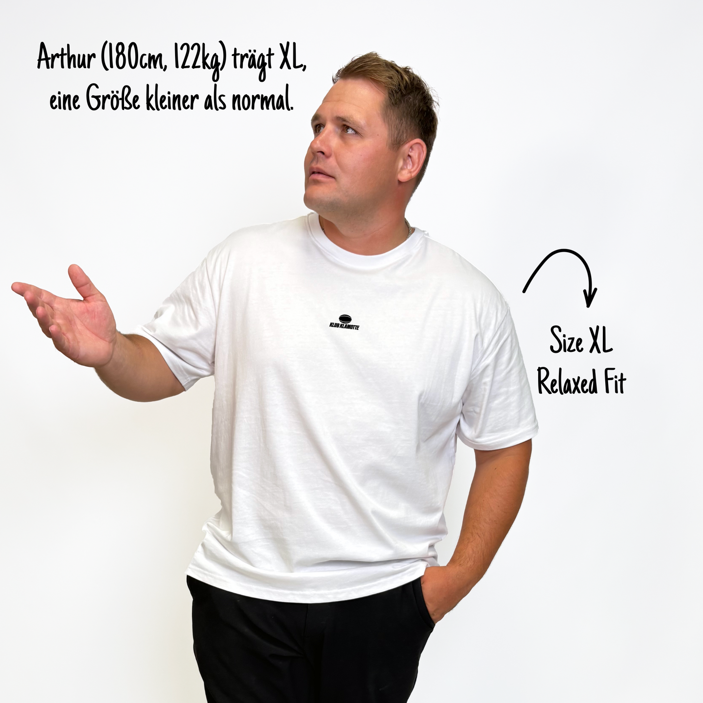 Arthur (180cm, 122kg) trägt das weiße Klub Streets Tee in XL. Man sieht das Model von vorne. Er trägt das Shirt im Relaxed Fit, eine Größe kleiner als normal. Das Shirt hat einen kleinen schwarzen Print auf der Brust: ein quer liegender Rugby Ball, darunter der Schriftzug Klub Klamotte.