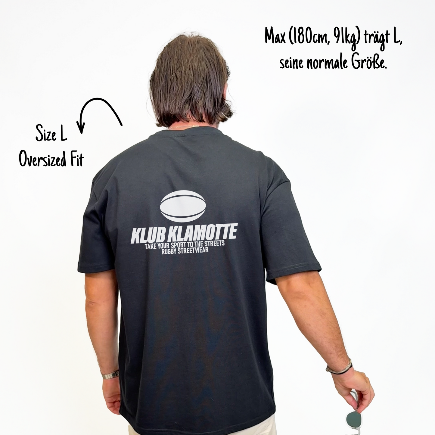 Max (180cm, 91kg) trägt das schwarze Klub Streets Tee in L. Man sieht das Model von hinten. Das Shirt ist oversized geschnitten und hat einen großen weißen Print auf dem Rücken: ein quer liegender Rugby Ball, darunter der Schriftzug Klub Klamotte und darunter "Take your sport to the streets, Rugby Streetwear".