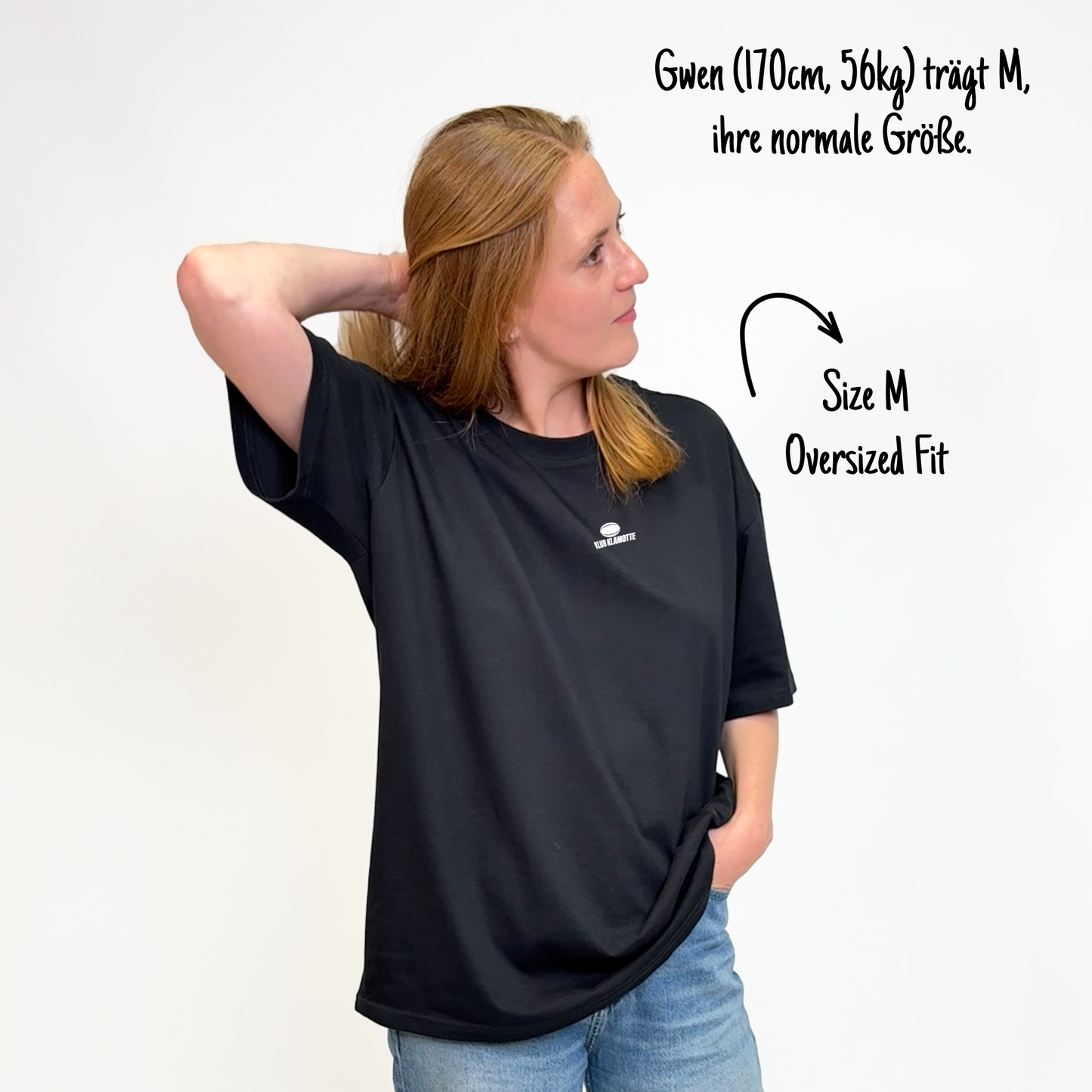 Gwen (170cm, 56kg) trägt das schwarze The Streets Tee in M. Man sieht das Model von vorne. Das Shirt ist oversized geschnitten und hat einen kleinen weißen Print auf der Brust: der Schriftzug Klub Klamotte und darüber ein quer liegender Rugby Ball.