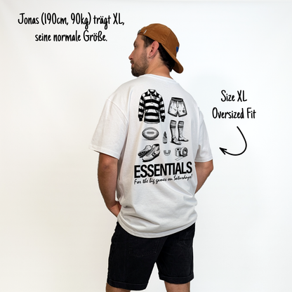 Jonas (190cm, 90kg) trägt das weiße The Essentials Tee in XL. Man sieht das Model von hinten. Das Shirt ist oversized geschnitten und hat einen großen Print auf dem Rücken: ein Trikot, Shorts, ein Ball, Schuhe, Mundschutz, Tape, Teebaumöl und Stulpen. Untendrunter steht: "Essentials for the big games on Saturdays!"