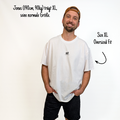 Jonas (190cm, 90kg) trägt das weiße The Essentials Tee in XL. Man sieht das Model von vorne. Das Tee hat einen kleinen Print auf der Brust: die Rugbyschuhe vom hinteren Print als Detail, darunter der Schriftzug Klub Klamotte.
