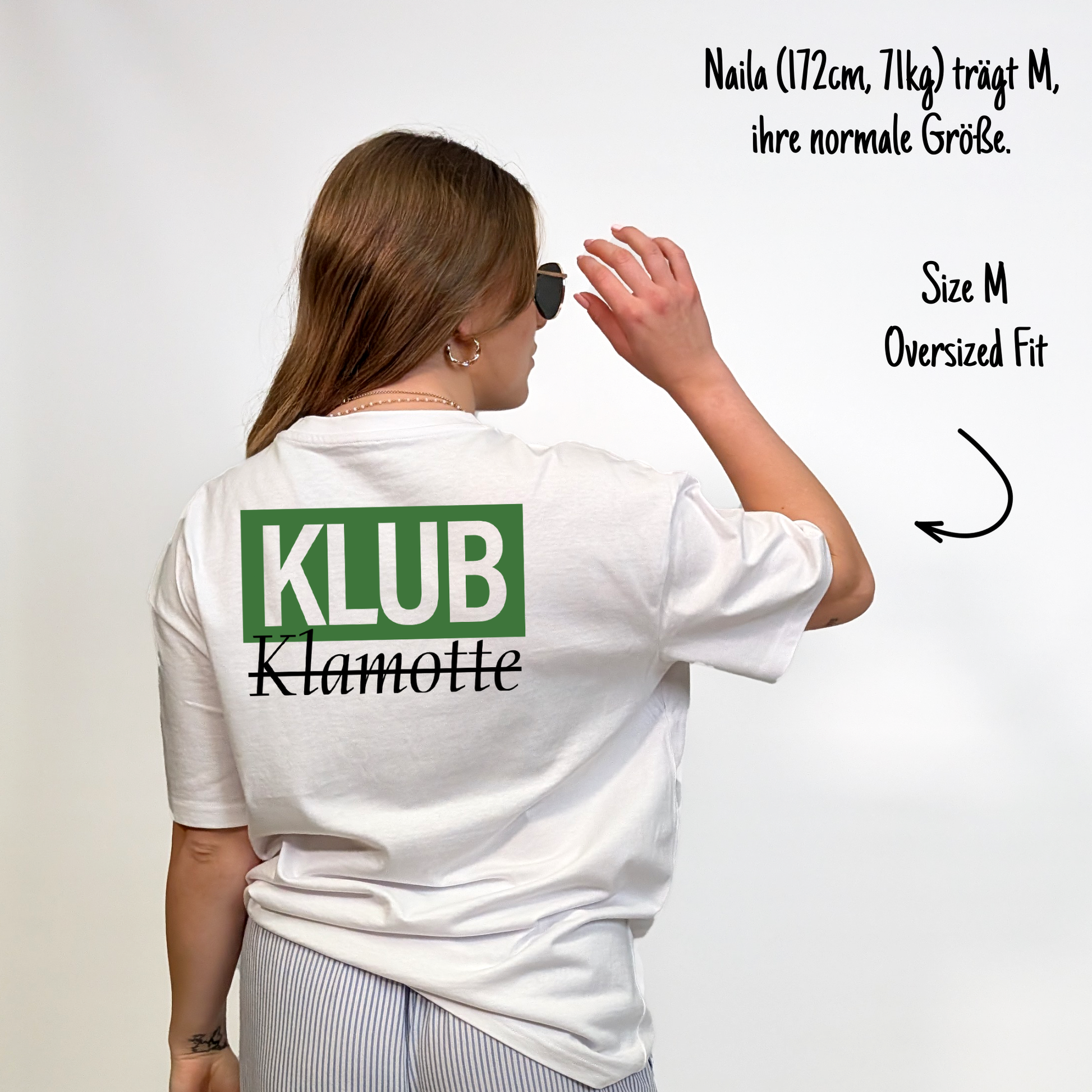 Naila (172cm, 71kg) trägt das weiße Klub Font Tee in M. Man sieht das Model von hinten. Sie trägt das Shirt im oversized Fit, ihre normale Größe. Das Shirt hat einen großen Print auf dem Rücken:  Ein grünes Rechteck mit dem weißen Schriftzug "KLUB" und darunter in schwarzer Schrift und durchgestrichen Klamotte.