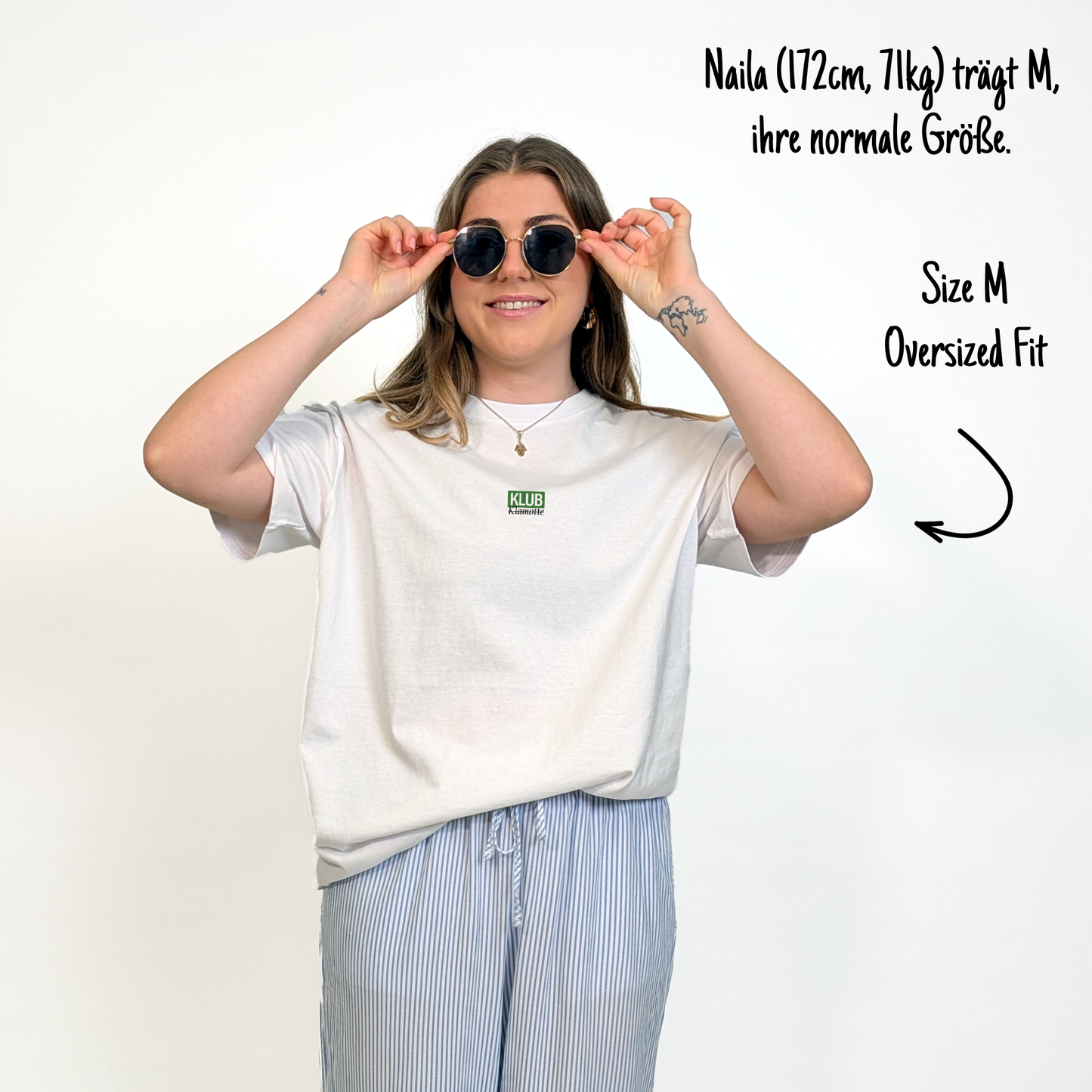 Naila (172cm, 71kg) trägt das weiße Klub Font Tee in M. Man sieht das Model von vorne. Sie trägt das Shirt im oversized Fit, ihre normale Größe. Das Shirt hat einen kleinen mittigen Print auf der Brust:  Ein grünes Rechteck mit dem weißen Schriftzug "KLUB" und darunter in schwarzer Schrift und durchgestrichen Klamotte.