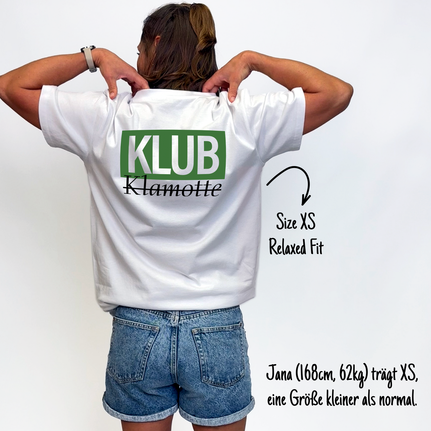 Jana (168cm, 62kg) trägt das weiße Klub Font Tee in XS. Man sieht das Model von hinten. Sie trägt das Shirt im Relaxed Fit, eine Größe kleiner als normal. Das Shirt hat einen großen Print auf dem Rücken:  Ein grünes Rechteck mit dem weißen Schriftzug "KLUB" und darunter in schwarzer Schrift und durchgestrichen Klamotte.
