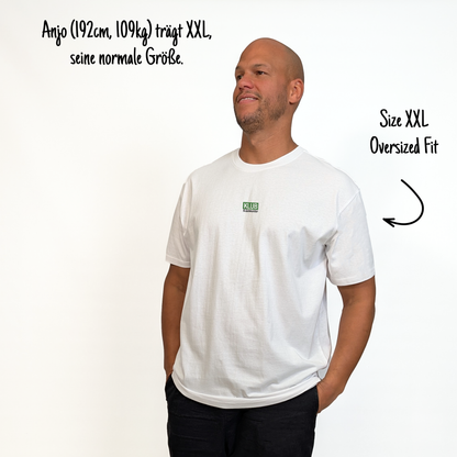 Anjo (192cm, 109kg) trägt das weiße Klub Font Tee in XXL. Man sieht das Model von vorne. Das Shirt ist oversized geschnitten und hat einen kleinen Print auf der Brust: das Wort KLUB in einem grünen Rechteck hinterlegt und darunter in Schwarz und durchgestrichen Klamotte.
