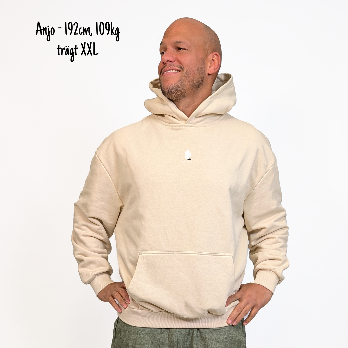 Anjo (192cm, 109kg) trägt den sandfarbenen From Klub to Pub Hoodie in XXL. Man sieht das Model von vorne. Der Hoodie hat einen kleinen Print auf der Brust: das Klub Klamotte Logo. 