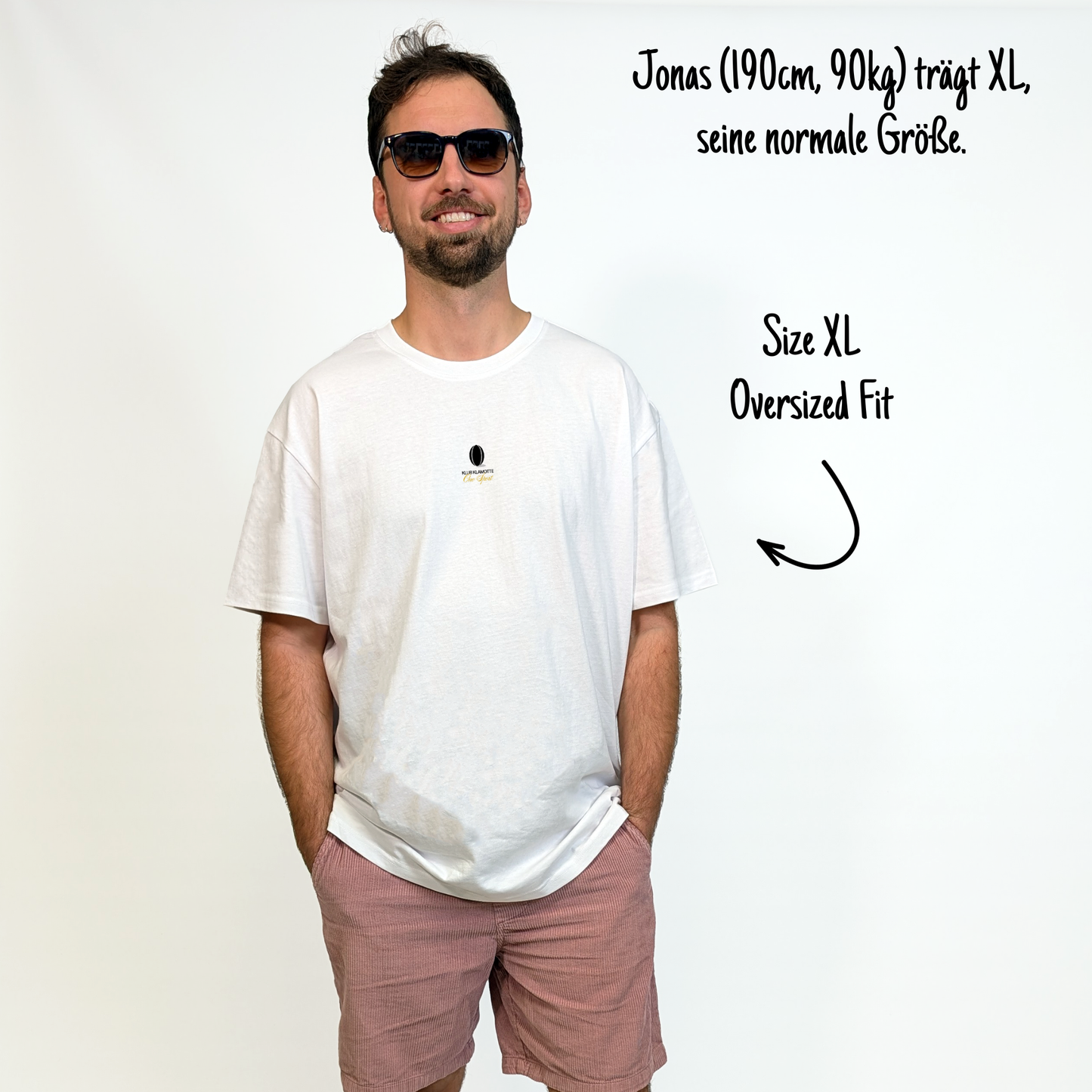 Jonas (190cm, 90kg) trägt das weiße One League Tee in XL. Man sieht das Model von vorne. Das Shirt ist oversized geschnitten und hat einen kleinen schwarzen Print auf der Brust: das Klub Klamotte Logo. Darunter in goldener kalligraphischer Schrift One Sport.
