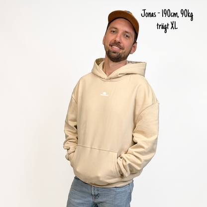 Jonas (190cm, 90kg) trägt den sandfarbenen Klub Streets Hoodie in XL. Man sieht das Model von vorne. Der Hoodie hat einen kleinen Print auf der Brust: ein quer liegender Rugby Ball, darunter der Schriftzug Klub Klamotte.