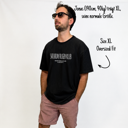 onas (190cm, 90kg) trägt das schwarze Klub Tee in XL. an sieht das Model von vorne. Das Shirt ist relaxed geschnitten und hat einen Print auf der Brust: Saturday Rugby Klub - More then a club a society.