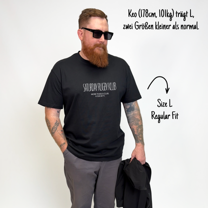 Keo (178cm, 101kg) trägt das schwarze Klub Tee in XL. Man sieht das Model von vorne. Das Shirt ist relaxed geschnitten und hat einen Print auf der Brust: Saturday Rugby Klub - More then a club a society.