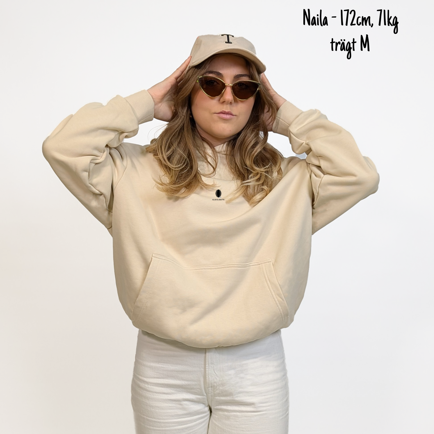 Naila (172cm, 71kg) trägt den sandfarbenen Slow Sunday Rugby Club Hoodie in M. Man sieht das Model von vorne. Der Hoodie hat einen kleinen Print auf der Brust: das Klub Klamotte Logo. 