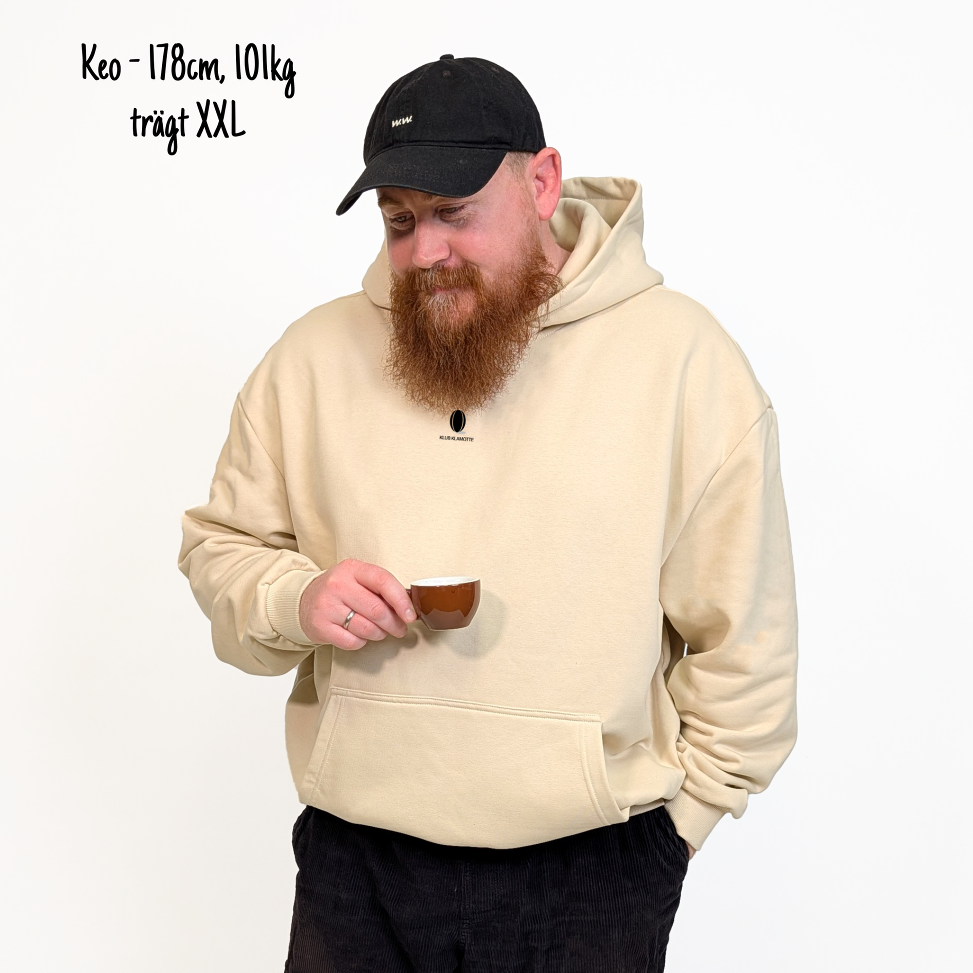 Keo (178cm, 101kg) trägt den sandfarbenen Slow Sunday Rugby Club Hoodie in XXL. Man sieht das Model von vorne. Der Hoodie hat einen kleinen Print auf der Brust: das Klub Klamotte Logo. 