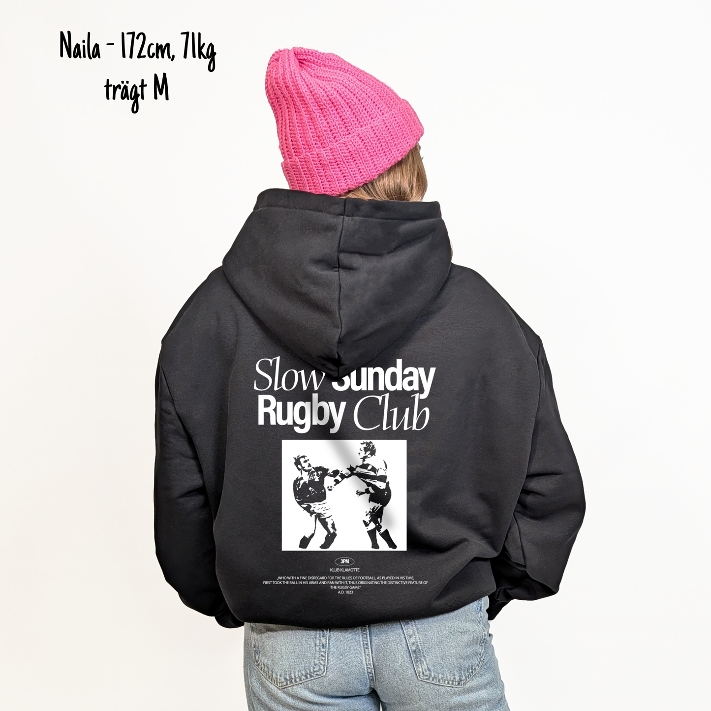 Naila (172cm, 71kg) trägt den schwarzen Slow Sunday Rugby Club Hoodie in M. Man sieht das Model von hinten. Der Hoodie hat einen großen Print auf dem Rücken: der Schriftzug Slow Sunday Rugby Club Tee und zwei Rugbyspieler im Streit. 