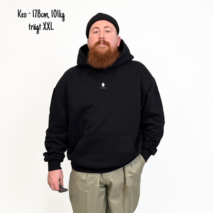 Keo (178cm, 101kg) trägt den schwarzen Slow Sunday Rugby Club Hoodie in XXL. Man sieht das Model von vorne. Der Hoodie hat einen kleinen Print auf der Brust: das Klub Klamotte Logo. 