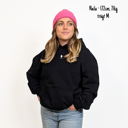 Naila (172cm, 71kg) trägt den schwarzen Slow Sunday Rugby Club Hoodie in M. Man sieht das Model von vorne. Der Hoodie hat einen kleinen Print auf der Brust: das Klub Klamotte Logo.