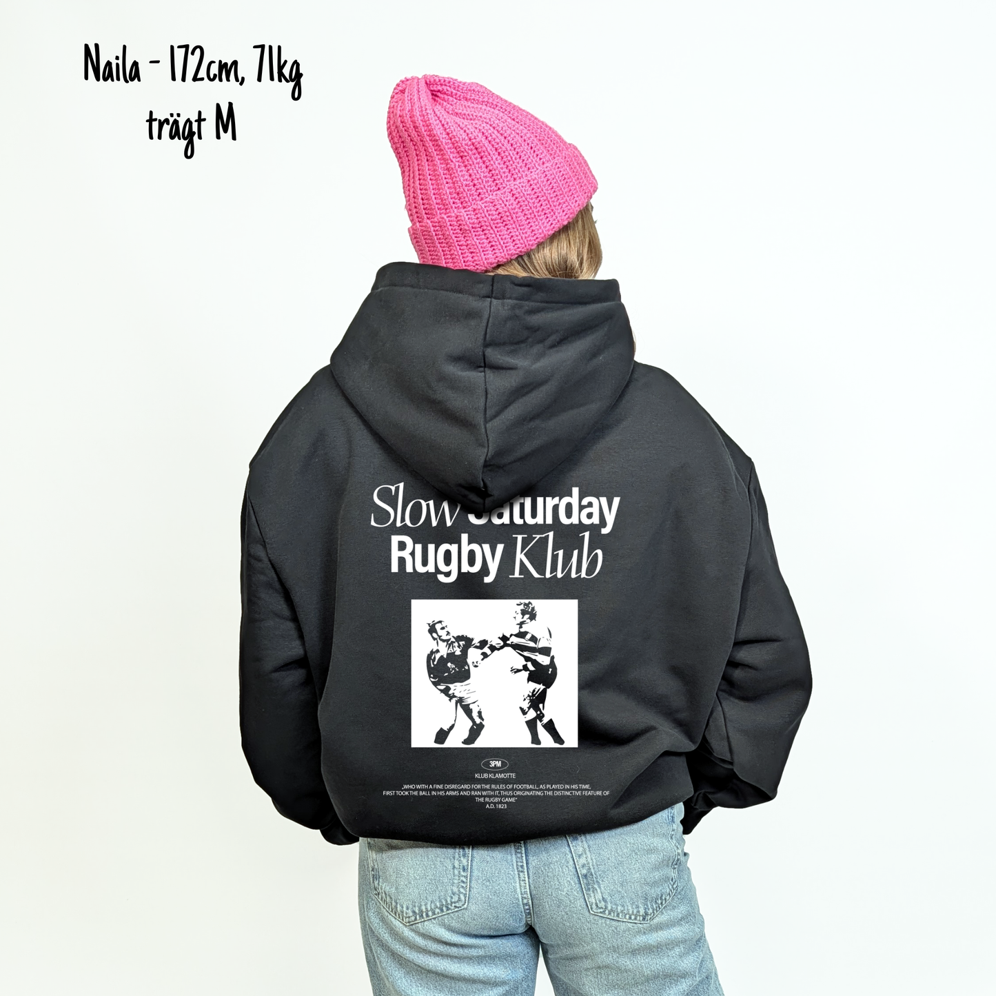 Naila (172cm, 71kg) trägt den schwarzen Slow Sunday Rugby Klub Hoodie in M. Man sieht das Model von hinten. Der Hoodie hat einen großen Print auf dem Rücken: der Schriftzug Slow Sunday Rugby Klub Tee und zwei Rugbyspieler im Streit. 