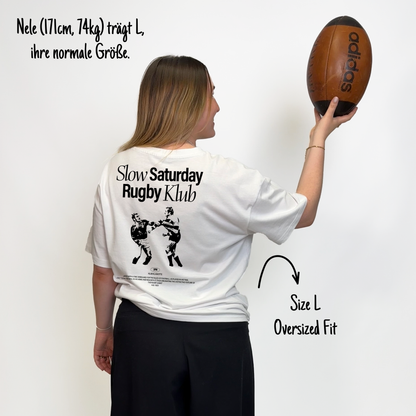 Nele (171cm, 74kg) trägt das weiße The Slow Sunday Rugby Klub Tee in L. Man sieht das Model von hinten. Das Shirt ist oversized geschnitten und hat einen großen Print auf dem Rücken: der Schriftzug Slow Sunday Rugby Klub Tee und zwei Rugbyspieler im Streit. 