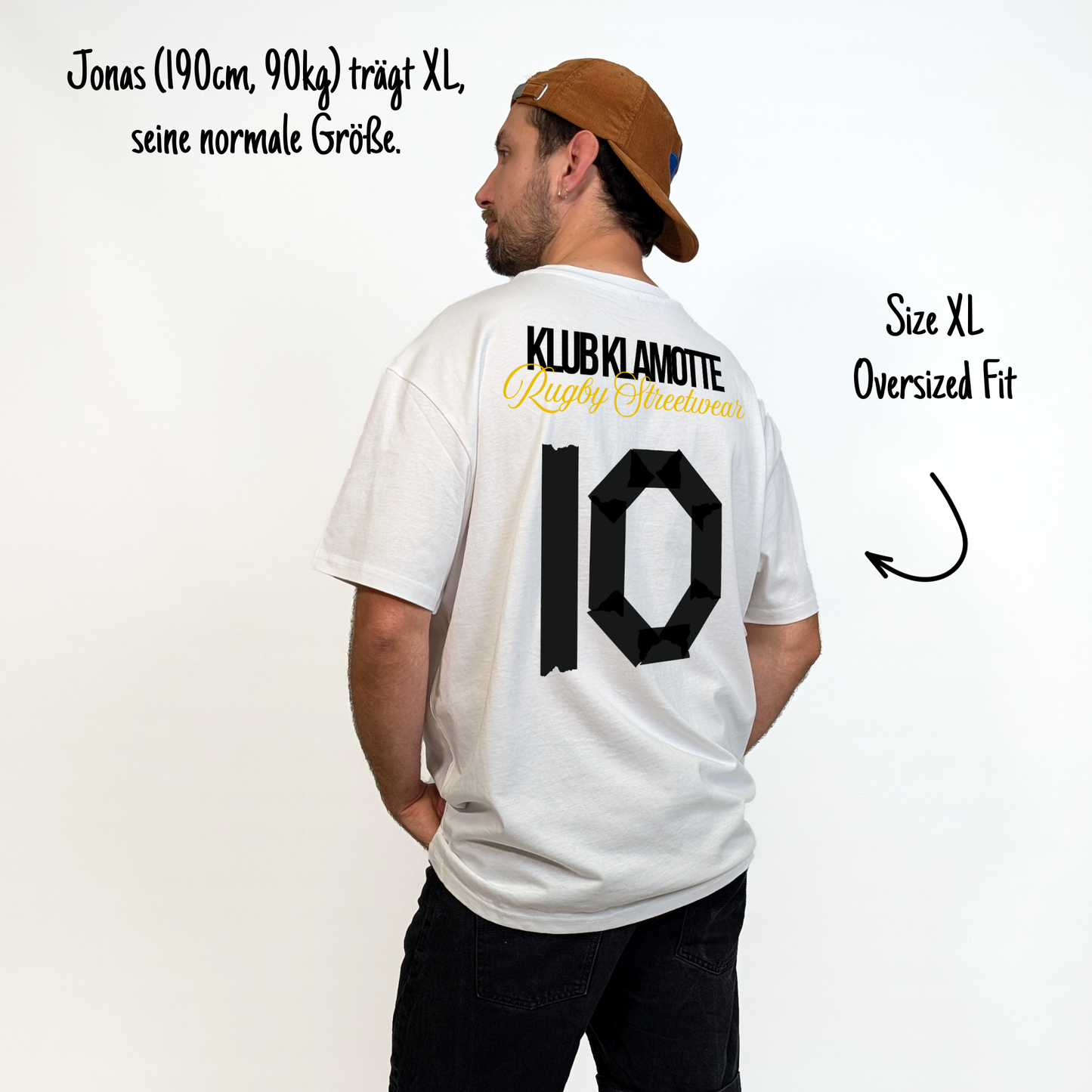Jonas (190 cm, 90 kg) trägt das weiße Team XV Tee in Größe XL. Das Model ist von hinten zu sehen. Das Shirt ist oversized geschnitten und hat einen großen schwarzen Rückendruck mit der Nummer 10 in Tape-Optik. Darüber steht „Klub Klamotte“ in Schwarz und „Rugby Streetwear“ in Gold.