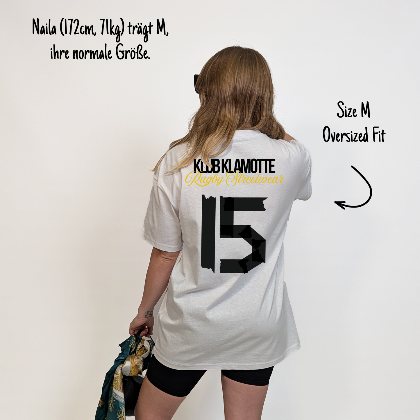Naila (172 cm, 71 kg) trägt das weiße Team XV Tee in Größe M. Das Model ist von hinten zu sehen. Das Shirt ist oversized geschnitten und hat einen großen schwarzen Rückendruck mit der Nummer 15 in Tape-Optik. Darüber steht „Klub Klamotte“ in Schwarz und „Rugby Streetwear“ in Gold.