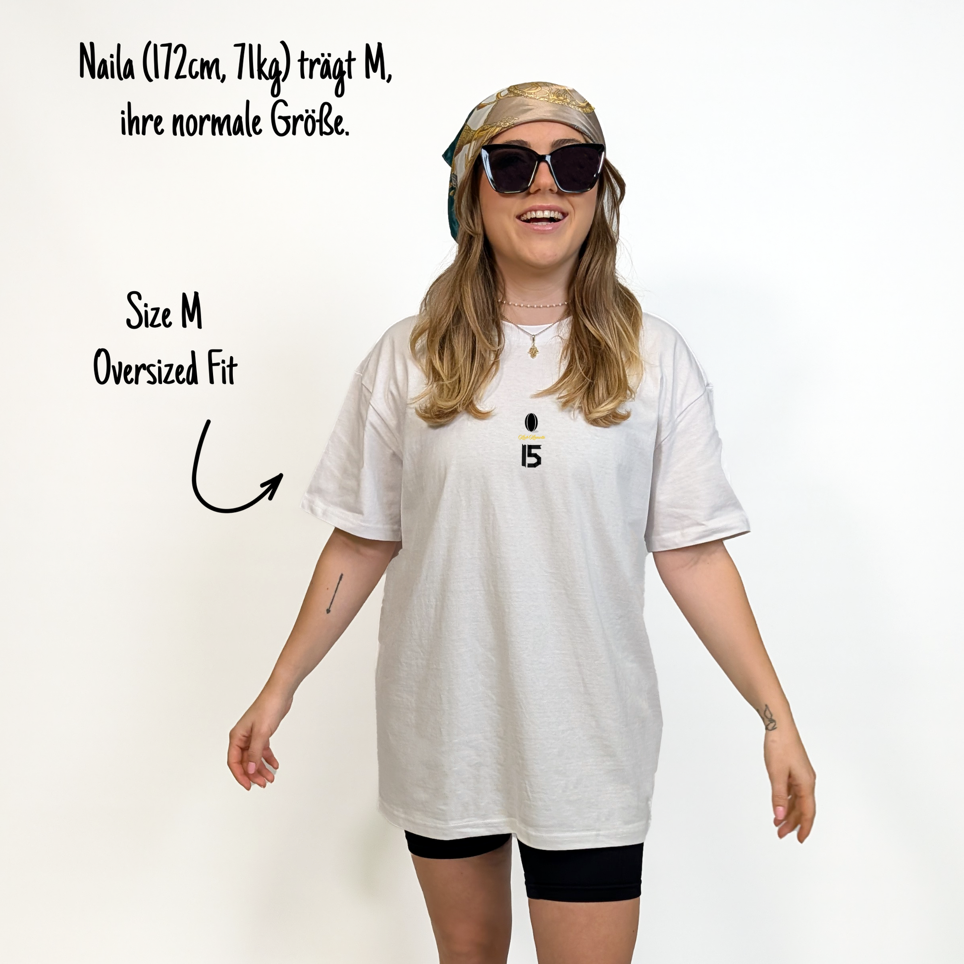 Naila (172 cm, 71 kg) trägt das weiße Team XV Tee in Größe M. Das Model ist von vorne zu sehen. Das Shirt ist oversized geschnitten und hat mittig auf der Brust einen kleinen Print mit einem schwarzen Rugbyball, dem goldenen Schriftzug „Klub Klamotte“ und der schwarzen Nummer 15 in Tape-Optik.