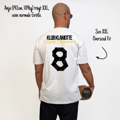 Anjo (192 cm, 109 kg) trägt das weiße Team XV Tee in Größe XXL. Das Model ist von hinten zu sehen. Das Shirt ist oversized geschnitten und hat einen großen schwarzen Rückendruck mit der Nummer 8 in Tape-Optik. Darüber steht „Klub Klamotte“ in Schwarz und „Rugby Streetwear“ in Gold.