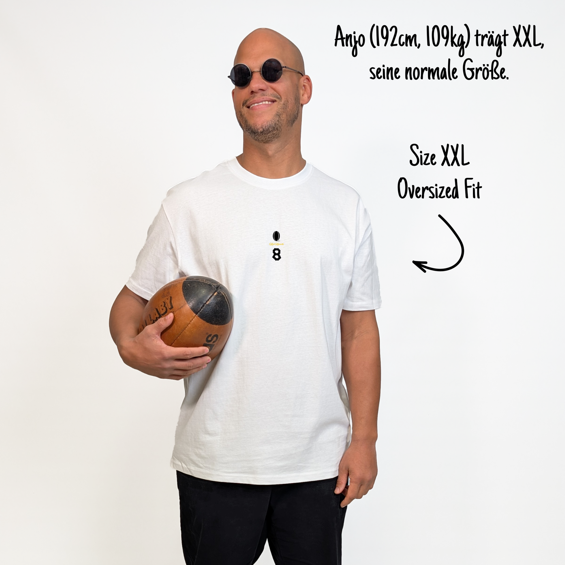 Anjo (192 cm, 109 kg) trägt das weiße Team XV Tee in Größe XXL. Das Model ist von vorne zu sehen. Das Shirt ist oversized geschnitten und hat mittig auf der Brust einen kleinen Print mit einem schwarzen Rugbyball, dem goldenen Schriftzug „Klub Klamotte“ und der schwarzen Nummer 8 in Tape-Optik.

