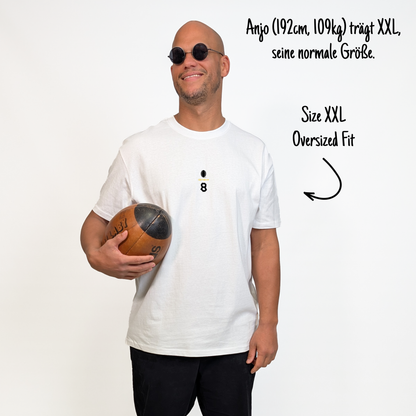 Anjo (192 cm, 109 kg) trägt das weiße Team XV Tee in Größe XXL. Das Model ist von vorne zu sehen. Das Shirt ist oversized geschnitten und hat mittig auf der Brust einen kleinen Print mit einem schwarzen Rugbyball, dem goldenen Schriftzug „Klub Klamotte“ und der schwarzen Nummer 8 in Tape-Optik.

